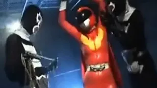 Sexy Super Hero in orange latex is strung up and tortured b