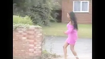 The girl in pink pissing standing against a brick wall